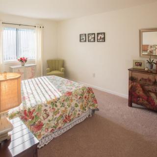 A cozy bedroom with floral bedspread, dresser, and window letting in natural light.