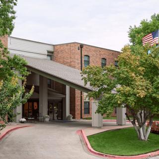 Entrance of a brick hospital building with trees and an American flag.