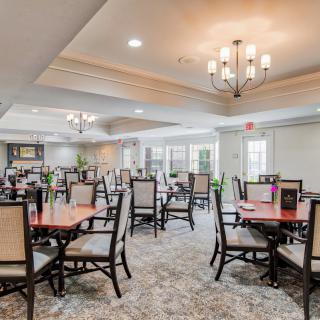 A spacious dining area with elegantly set tables and comfortable seating, illuminated by chandeliers.