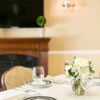 An elegantly set dining table with floral centerpiece and glassware, positioned in a cozy room with a fireplace.