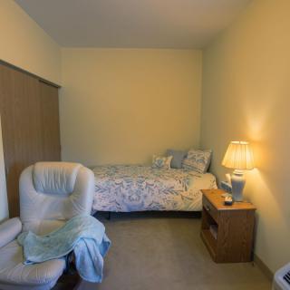 A cozy bedroom with a bed, chair, and nightstand featuring a lamp.