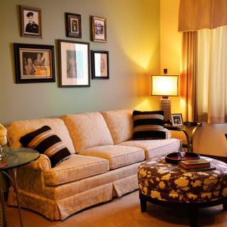 A cozy living room with a beige sofa, patterned ottoman, and decorative wall art.