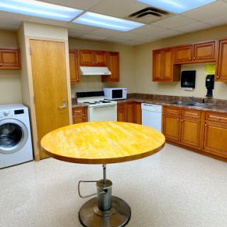A tidy kitchen area featuring wooden cabinets, a central table, and laundry facilities.