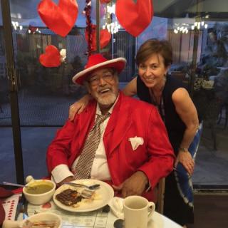 A joyful moment captured as a couple enjoys a meal at a restaurant, with one person dressed in a vibrant red outfit and both smiling warmly.