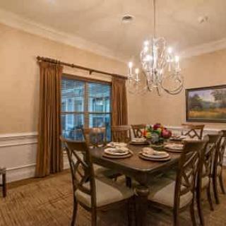 A warmly lit dining room featuring a wooden table set for dinner, surrounded by chairs and illuminated by an elegant chandelier.