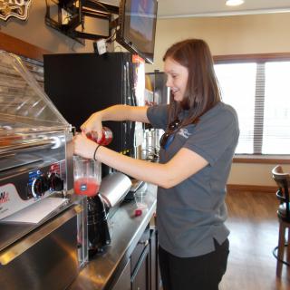 A woman in uniform preparing a beverage at a restaurant counter.