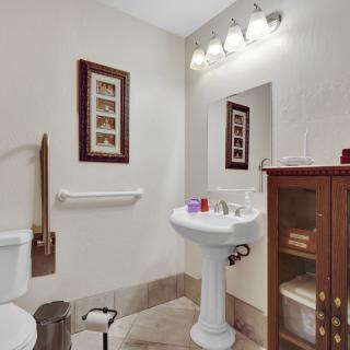 A well-lit bathroom with a pedestal sink, toilet, wooden cabinet, and wall art.