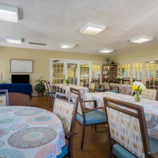 A well-lit dining room with multiple tables and chairs, featuring decorative elements and indoor plants.