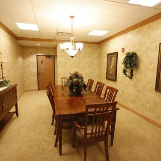 A formal dining room with a wooden table and matching chairs, decorated with artwork and greenery.