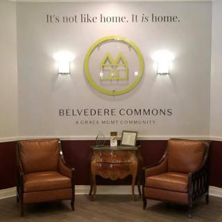 A cozy seating area with two chairs and a table beneath a wall-mounted logo of Belvedere Commons.