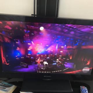 A vibrant concert performance on stage with colorful lighting, viewed on a television screen.