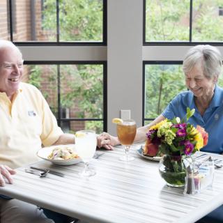 An elderly couple enjoying a meal together at a restaurant, sitting at a table with colorful flowers.