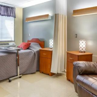 A clean and well-lit hospital room with a bed, bedside tables, and comfortable seating.