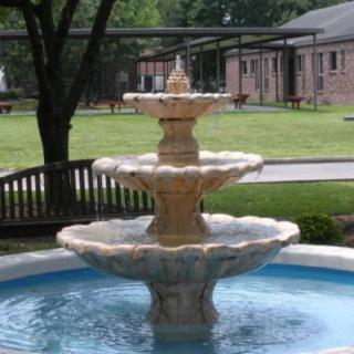 A tiered fountain in a park setting with buildings and trees in the background.