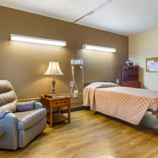 A well-lit patient room featuring a bed, recliner chair, and comfortable furnishings.