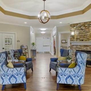 A cozy living room with patterned chairs, a stylish chandelier, and a stone fireplace.