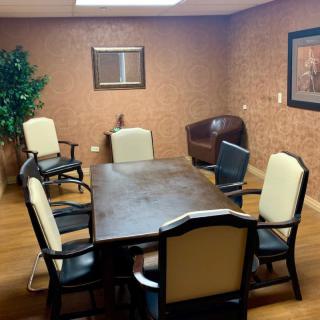 A small conference room with a wooden table and six chairs, decorated with artwork and a potted plant.