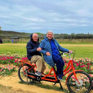 A joyful couple enjoying a ride on a tandem bike amidst blooming flowers.