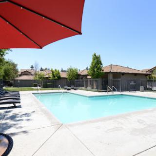 A refreshing swimming pool surrounded by lounge chairs and a vibrant red umbrella, perfect for summer relaxation.