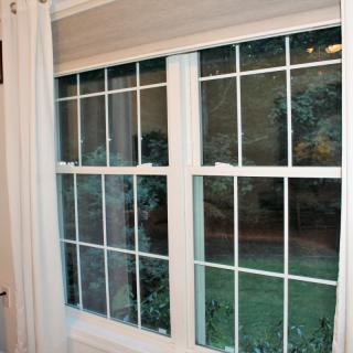 A view of a double-paneled window with white grid patterns, framed by light curtains, showing an evening scene outside.