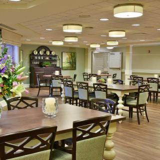 A well-lit dining room with neatly arranged tables and chairs, featuring floral decorations.