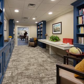 A cozy hallway with blue bookshelves, seating, and a globe, leading to another room.