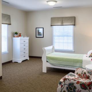 A simple and cozy bedroom with a bed, dresser, and windows covered with blinds.