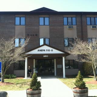 A photo of a multi-story building with an entrance sign, surrounded by small trees.