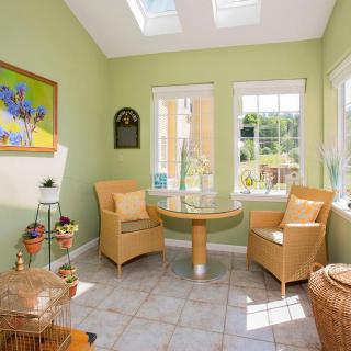 A bright sunroom featuring wicker chairs and a glass table, with natural light streaming in through skylights and windows.