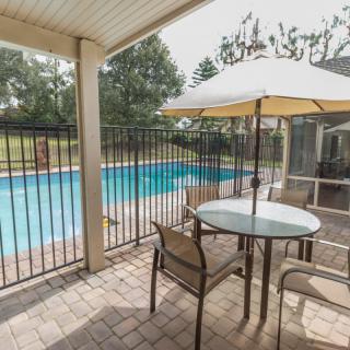 A cozy patio area with a table and chairs overlooks a backyard pool, surrounded by a safety fence and shaded by an umbrella.