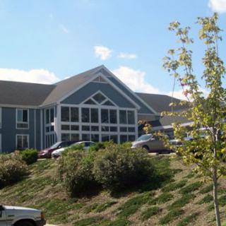 A suburban house with a sloped grassy lawn and parked cars under a clear blue sky.