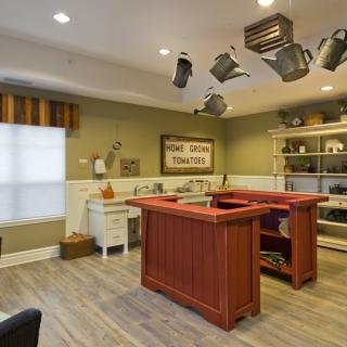 A cozy kitchen featuring a central island counter with hanging pots and pans, wooden flooring, and neatly organized shelves.