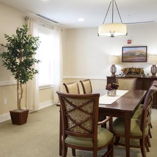 A well-lit dining room with a wooden table, chairs, a potted plant, and wall decor.