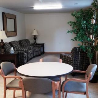A cozy living room with seating area, a round table surrounded by chairs, and decorative elements like a lamp and a large indoor plant.