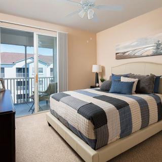 A cozy bedroom with a striped bedspread, a large window leading to a balcony, and calming decor.