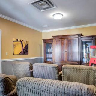 A cozy living room with several chairs, a wooden cabinet, and a piece of artwork on the wall.