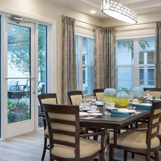 A modern dining room with a large table and chairs, surrounded by windows allowing in natural light.