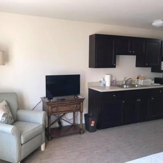 A cozy living area with a compact kitchen, featuring dark cabinets, a television on a wooden stand, and a comfortable armchair.