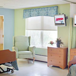 A hospital room with a bed, chair, dresser, and television.