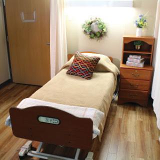 A cozy and well-organized patient room featuring a hospital bed, wooden furniture, and warm decor.