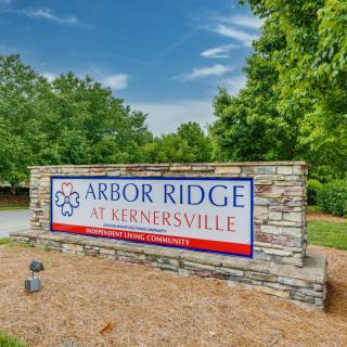 A stone sign for Arbor Ridge at Kernersville surrounded by trees and a clear blue sky.