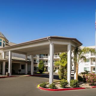 A modern building entrance with a covered driveway and landscaped surroundings under a clear blue sky.