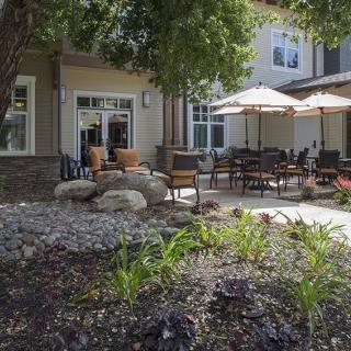 A cozy outdoor patio area with chairs and umbrellas surrounded by a landscaped garden.