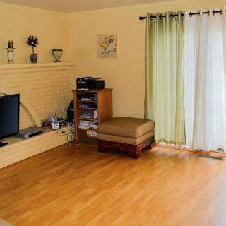 A minimalist living room featuring a wooden floor, television, shelving, and green curtains.