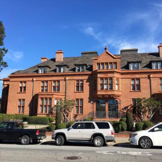 A historic brick building with parked cars in front on a sunny day.