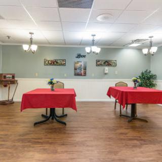 A spacious restaurant interior featuring two tables with red tablecloths, decorative artwork on the walls, and warm lighting.