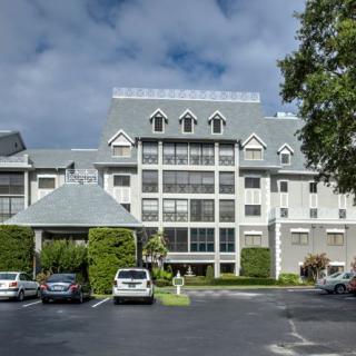A large hotel building with a parking lot in front, surrounded by trees under a partly cloudy sky.