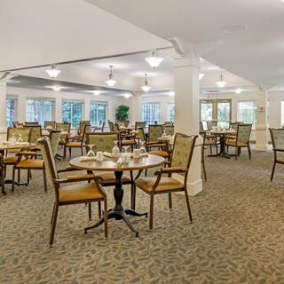 An empty dining room with neatly arranged tables and chairs, illuminated by overhead lights.