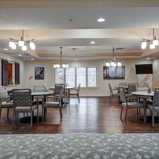 A spacious dining room with neatly arranged tables and chairs, featuring elegant lighting and large windows.