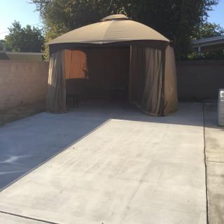 A backyard patio with a gazebo providing shade over a concrete area.